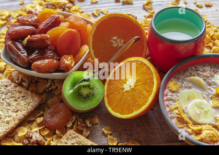 Petit-déjeuner de céréales avec du lait et de la banane, orange, kiwi et les prunes séchées servi dans des bols Banque D'Images