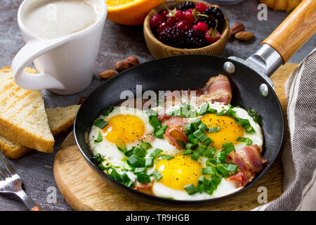 Petit-déjeuner d'œufs brouillés avec du bacon, du café, des petits fruits, des biscuits, des noix et du jus sur dark surface de la table. Banque D'Images