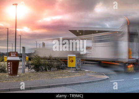 Un grand camion articulé tire sur une avant-cour garage, comme le soleil illumine les nuages de tempête rassemblement dans le ciel au-dessus. Banque D'Images