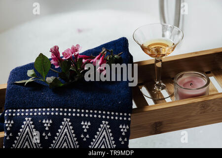 étagère en bois sur la baignoire avec verre de vin blanc, fleurs roses et accessoires de bain naturels Banque D'Images