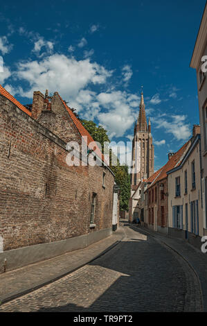 Long mur de briques, tour et maisons sous ciel bleu sur la rue du centre-ville de Bruges. Charmante ville avec des canaux et de vieux bâtiments en Belgique. Banque D'Images