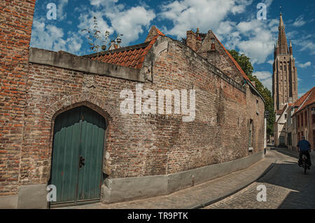 Long mur de briques, tour et maisons sous ciel bleu sur la rue du centre-ville de Bruges. Charmante ville avec des canaux et de vieux bâtiments en Belgique. Banque D'Images