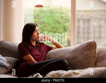 Teen girl Biracial les jambes jusqu'à l'emplacement sur la table gris à grande fenêtre, pensant Banque D'Images