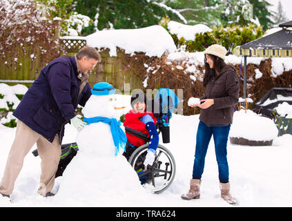 Personnes handicapées en fauteuil roulant biracial jeune garçon avec un bonhomme de père et sa soeur en hiver après les fortes chutes de neige Banque D'Images