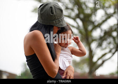 Jeune mère portant son joli jolie petite fille dans le parc au soleil d'été Banque D'Images