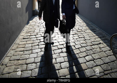Deux fonctionnaires en costumes noirs marcher ensemble pour travailler dans de longues ombres tôt le matin Banque D'Images