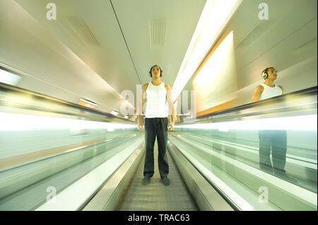 Amazing shot d'un homme moderne debout sur un escalier mécanique en mouvement portant des écouteurs et écouter de la musique Banque D'Images