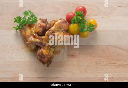 Ailes de poulet épicées juteux cuits au four avec tomates jaune et rouge et persil frais sur une planche en bois Banque D'Images