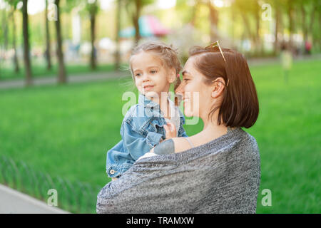 Un peu Caucasian girl vêtu d'une veste en jean se trouve dans les bras de sa mère. Maman et sa fille dans le parc du Golfe sur une chaude journée d'été vie Banque D'Images