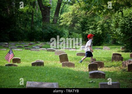 Plymouth Meeting, PA, USA - juin 1, 2019 : un jeune garçon, en bonnet rouge passe entre tombes cimetière Quaker. Banque D'Images