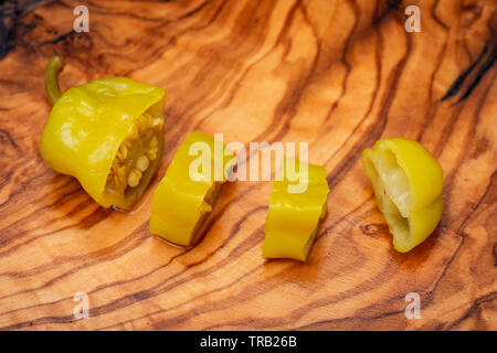 Or, poivrons marinés grecque ou Friggitelli Pepperoncini (piment sucré italien) sur une planche à découper en bois d'olivier naturel . Capsicum annuum. Banque D'Images