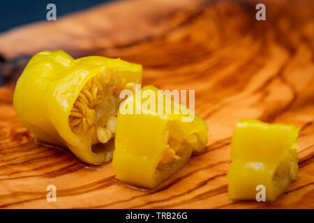 Or, poivrons marinés grecque ou Friggitelli Pepperoncini (piment sucré italien) sur une planche à découper en bois d'olivier naturel . Capsicum annuum. Banque D'Images