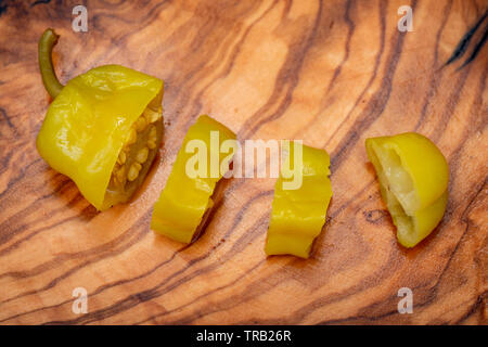 Or, poivrons marinés grecque ou Friggitelli Pepperoncini (piment sucré italien) sur une planche à découper en bois d'olivier naturel . Capsicum annuum. Banque D'Images