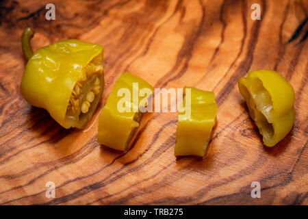 Or, poivrons marinés grecque ou Friggitelli Pepperoncini (piment sucré italien) sur une planche à découper en bois d'olivier naturel . Capsicum annuum. Banque D'Images