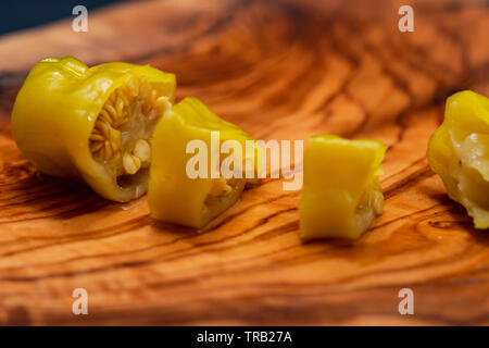 Or, poivrons marinés grecque ou Friggitelli Pepperoncini (piment sucré italien) sur une planche à découper en bois d'olivier naturel . Capsicum annuum. Banque D'Images