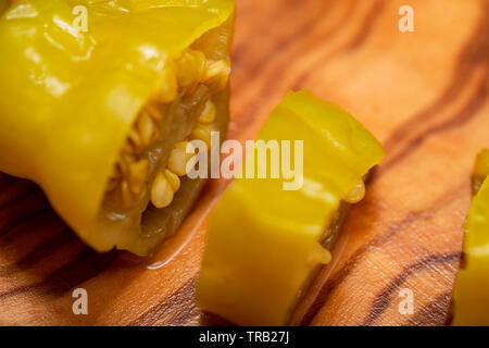 Or, poivrons marinés grecque ou Friggitelli Pepperoncini (piment sucré italien) sur une planche à découper en bois d'olivier naturel . Capsicum annuum. Banque D'Images