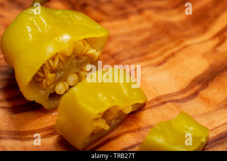 Or, poivrons marinés grecque ou Friggitelli Pepperoncini (piment sucré italien) sur une planche à découper en bois d'olivier naturel . Capsicum annuum. Banque D'Images