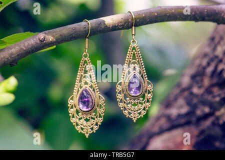 D'oreilles en métal laiton avec pierre naturelle Améthyste minéraux hanging on tree branch Banque D'Images