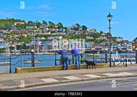 Un couple en train de marcher avec leur chien le long du front de mer de Dartmouth, l'arrêter pour profiter de la vue sur la rivière Dart pour le pittoresque village de Kingswear. Banque D'Images