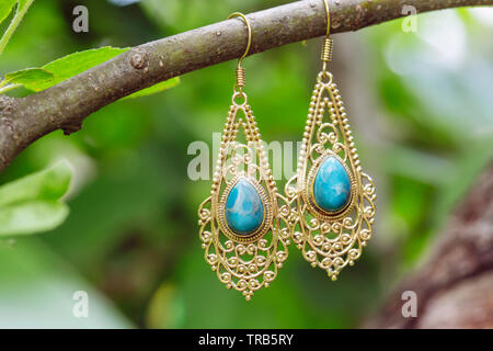 D'oreilles en métal laiton avec pierre larimar minérales naturelles hanging on tree branch Banque D'Images