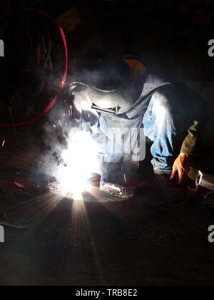 Close-up d'un homme habillé en jeans faisant un travail de soudure avec des étincelles voler autour, vu dans les Philippines Banque D'Images