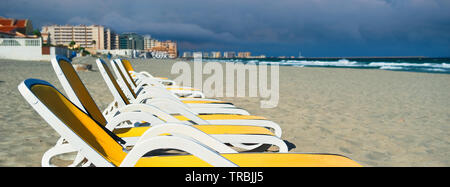 Image horizontale vue rognée jaune bleu chaises longues vides chaises longues dans une rangée sur la plage de sable, la Manga del Mar Menor bord de mer. Espana Banque D'Images