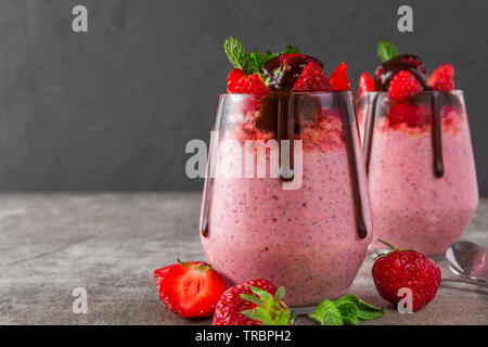 Deux verres de semence chia pudding aux fraises avec du chocolat, de baies fraîches et de menthe pour un délicieux petit-déjeuner sur fond de béton Banque D'Images