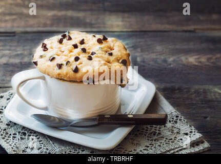 Des gâteaux frais dans une tasse avec du beurre d'arachides et de chocolat sur fond de bois rustique. Cuit dans un four micro-ondes. Banque D'Images