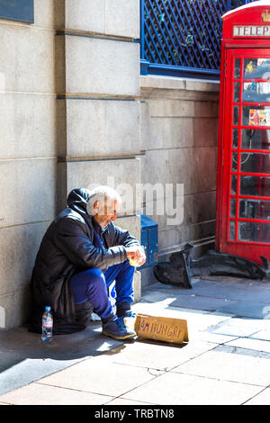 Faim sans-abri avec 'J'ai faim' assis sur le trottoir et de manger en face de l'Hôtel Ritz, Green Park, London, UK Banque D'Images