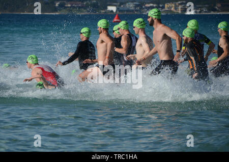 Les triathlètes masculins courir dans les vagues au début de plage Calalla triathlon. Les concurrents de l'endurance triathlon race dans l'océan. Banque D'Images
