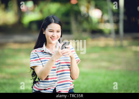 Belle asiatique femme heureuse et souriant / Jeunes filles étudiant femme jouant de l'utilisation de smartphone dans jardin parc extérieur Banque D'Images