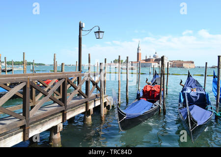 Une vue panoramique sur la lagune de Venise, San Giorgio Maggiore island, deux gondoles ancrées à des poteaux en bois, près de l'embarcadère en bois en journée ensoleillée. Banque D'Images