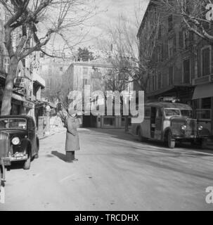 1950s, historique, France, Sisteron, vue sur une rue de la vieille ville, avec une voiture garée et un bus de l'époque, allant à digne. La voiture garée est dotée d'un badge sur son pare-chocs avant indiquant « Cinema Rallye Monte-Carlo ». Aussi dans l'image dans la distance est 'Galeries Sisteronais'. Une vieille ville, construite à l'origine au 11th siècle, avec des ajouts ultérieurs, elle se trouve entre les Alpes et la Méditerranée. Banque D'Images