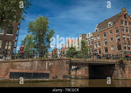 Les bâtiments de brique et de pont sur canal avec les vélos et ciel bleu ensoleillé à Amsterdam. L'activité culturelle de la ville avec d'énormes, les canaux et les ponts en Pays-Bas Banque D'Images