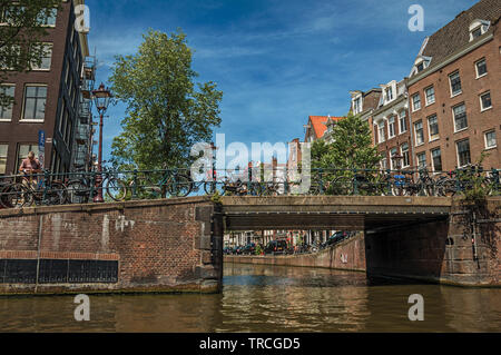 Les bâtiments de brique et de pont sur canal avec les vélos et ciel bleu ensoleillé à Amsterdam. L'activité culturelle de la ville avec d'énormes, les canaux et les ponts en Pays-Bas Banque D'Images