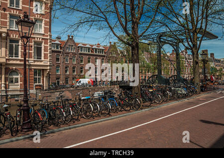 Park des vélos sur rue à côté canal et de vieux bâtiments en journée ensoleillée à Amsterdam. L'activité culturelle de la ville avec d'énormes, les canaux et les ponts en Pays-Bas. Banque D'Images