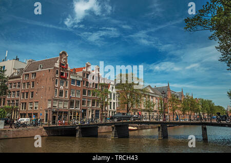 Canal avec bâtiments en brique, des vélos sur le pont et ciel bleu ensoleillé à Amsterdam. L'activité culturelle de la ville avec d'énormes, les canaux et les ponts en Pays-Bas. Banque D'Images