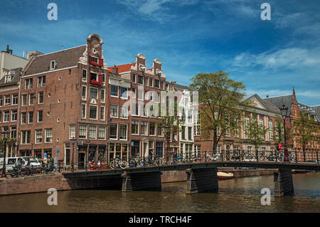 Canal avec bâtiments en brique, des vélos sur le pont et ciel bleu ensoleillé à Amsterdam. L'activité culturelle de la ville avec d'énormes, les canaux et les ponts en Pays-Bas. Banque D'Images