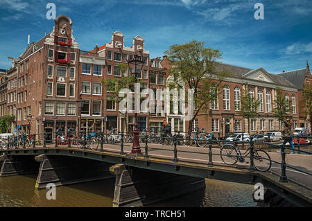 Canal avec bâtiments en brique, des vélos sur le pont et ciel bleu ensoleillé à Amsterdam. L'activité culturelle de la ville avec d'énormes, les canaux et les ponts en Pays-Bas. Banque D'Images