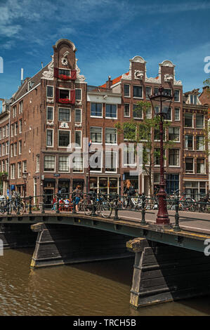 Canal avec bâtiments en brique, des vélos sur le pont et ciel bleu ensoleillé à Amsterdam. L'activité culturelle de la ville avec d'énormes, les canaux et les ponts en Pays-Bas. Banque D'Images