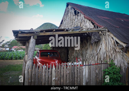 Classic, vintage voiture rouge l'article ci-dessous un carport en bois dans la célèbre destination touristique et du patrimoine de l'UNESCO la vallée de Vinales, Pinar del Rio, Cuba Banque D'Images