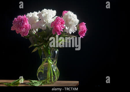 Un bouquet de pivoines blanches et rouges dans un vase transparent sur fond sombre Banque D'Images