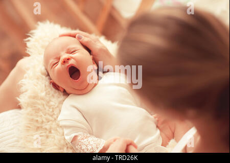 Le bâillement Cute infant baby sur les mères mains dans la chambre. La maternité. La maternité. L'enfance. Banque D'Images