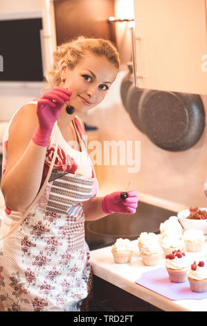 Smiling woman decorating cupcakes cuisine avec les baies fraîches dans la cuisine. En regardant la caméra. Banque D'Images