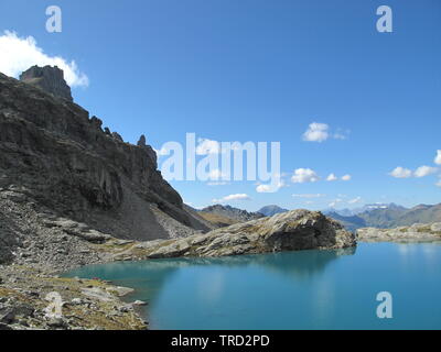 Les sommets des montagnes grises, le coton des nuages et un ciel bleu profond se reflètent dans le lac alpin turquoise ensoleillé Banque D'Images