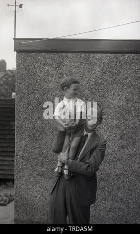 Années 1950, historiques, à l'extérieur, un père dans sa combinaison en tenant son fils sur son épaule, qui a dans ses mains sa peluche, un peu ours, England, UK. Banque D'Images