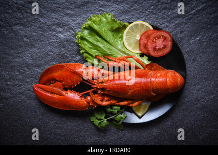 Sur la plaque du homard fruits de mer avec salade et légumes citron laitue tomate sur fond sombre Banque D'Images