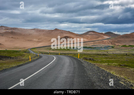 Route sinueuse, vide pré et montagnes rouges dans l'arrière-plan dans la région de Myvatn, ciel couvert jour en été Banque D'Images