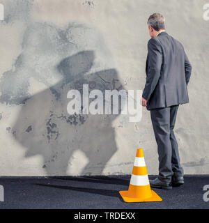 Vue arrière d'un épuisé business man standing motionlessly avec bras de suspension devant un mur gris Banque D'Images