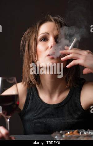 Portrait d'un déprimé et femme désalcoolisée avec un verre de vin et une cigarette dans ses mains Banque D'Images